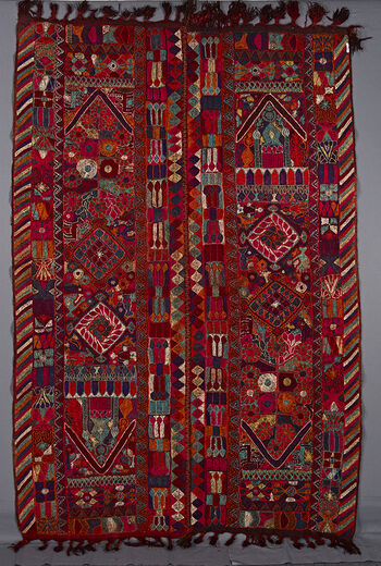 (UEM49202) The&amp;#160;cloth under the embroidery is somewhat darker than the other blankets in the series. The outer vertical border of each panel has the characteristic multi coloured diagonal lines pattern. In the centre of each panel running vertically are two big diamonds and a mosque or a house at one end. This latter motif is at diagonally opposite ends of the panels. Delimiting the ends of the two panels is a V motif like a roof. Additional motifs consisting of a profusion of living creatures: man, birds, fish, dogs, horses ,insects and so on. These are interspersed with vegetal and geometric motifs. The fringes are plaited. This blanket is especially bright and fresh.&amp;#160;