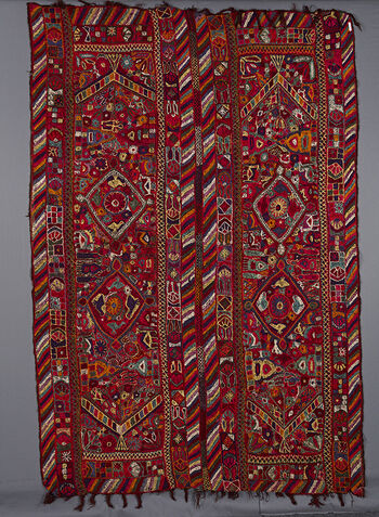 (UEM49206) The blanket is double bordered. There is the characteristic multi coloured diagonal lines pattern at the vertical edges of both panels. At both ends of each of the vertical panels there is a flowering plant which faces towards the centre and therefore limits the central area. In the centre are two diamond shaped motifs containing birds. In addition there is also a profusion of living creatures such as camels, birds, insects, architectoral motifs, as well as flowers and plants.&amp;#160;