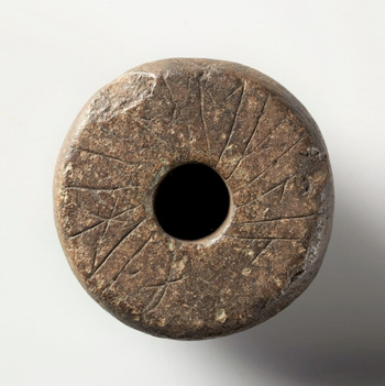 &quot;Halha · a snalt þenan&quot; says the inscription on this spindle-whorl of stone. In classical Old Norse this sounds Helga á snáld þenna, meaning “Helga owns this spindle-whorl”. The word snáldr refers to the spindle-whorl, still known in some Norwegian dialects as “snåld”. The inscription is from the late Viking Age or early Middle Ages. The object was found in the 1950s by teacher Jon T. Uppstad under the old smokehouse at Uppstad farm in Valle, Norway. Spindle-whorls were a common tool in the spinning of thread. Several runic inscriptions are known on spindle-whorls from Scandinavia and elsewhere. In this manner people could mark the practical tools in their everyday life. Runic signum: N 582. C28808.