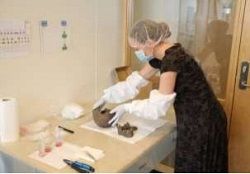forsker med munnbind, hårnett og hansker håndterer et arkeologisk objekt
