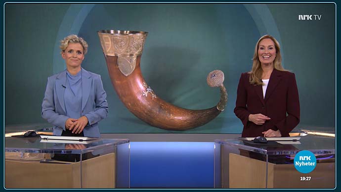 Skjermdump fra NRK Dagsrevyens tv-sending. To personer ser i kamera, bak stort bilde av kongshornet.